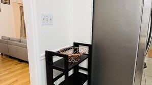 Une cuisine avec une  étagère en métal noir, un réfrigérateur en acier inoxydable et un canapé beige à l’arrière-plan.