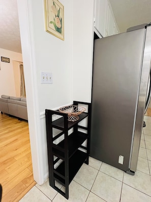A kitchen with a black metal shelf, a stainless steel refrigerator, and a beige sofa in the background.