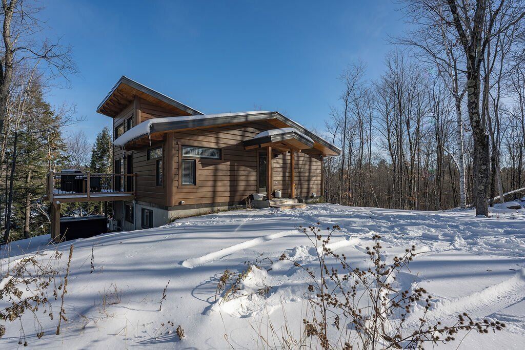 A log cabin with a covered porch, a second-story balcony, and a snow-covered landscape.