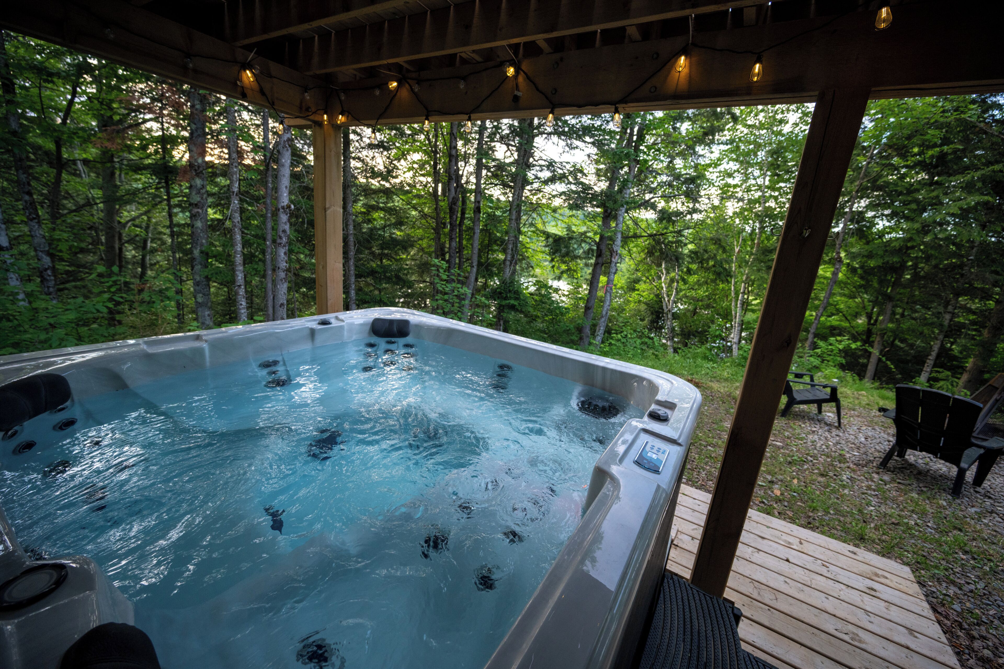 Un bain à remous situé dans un espace boisé, avec une terrasse en bois et des chaises.