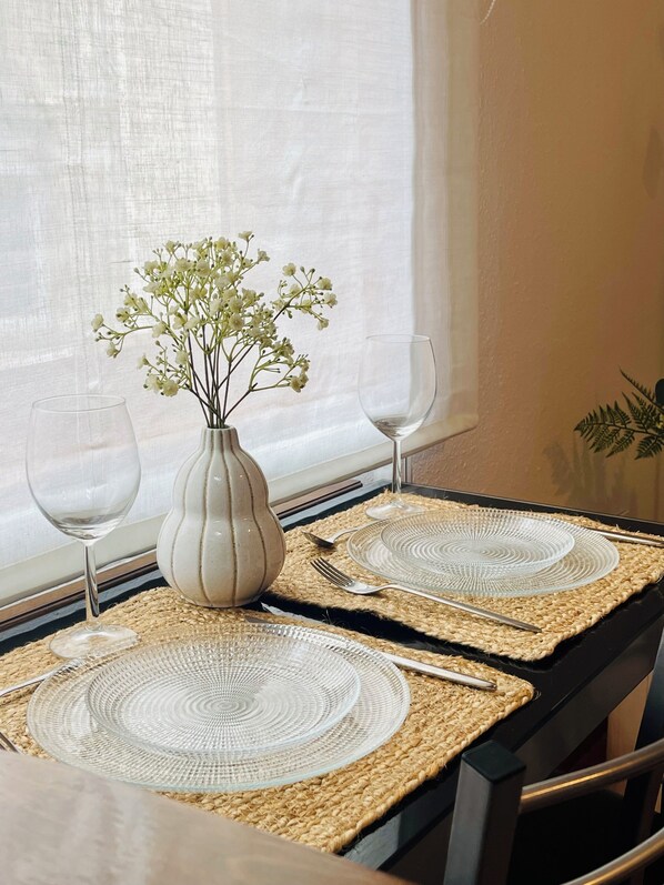A dining table with two glass plates, a vase with flowers, and a glass of water.