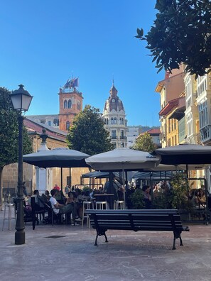 Ein Straßencafé mit Tischen und Bänken, umgeben von historischen Gebäuden und blauem Himmel.
