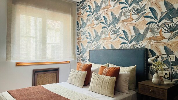 A bedroom with a bed, pillows, a bedside table with a lamp, a window with a sheer curtain, and a wall with a tropical leaf pattern. - Apartment San francisco Oviedo (Oviedo)