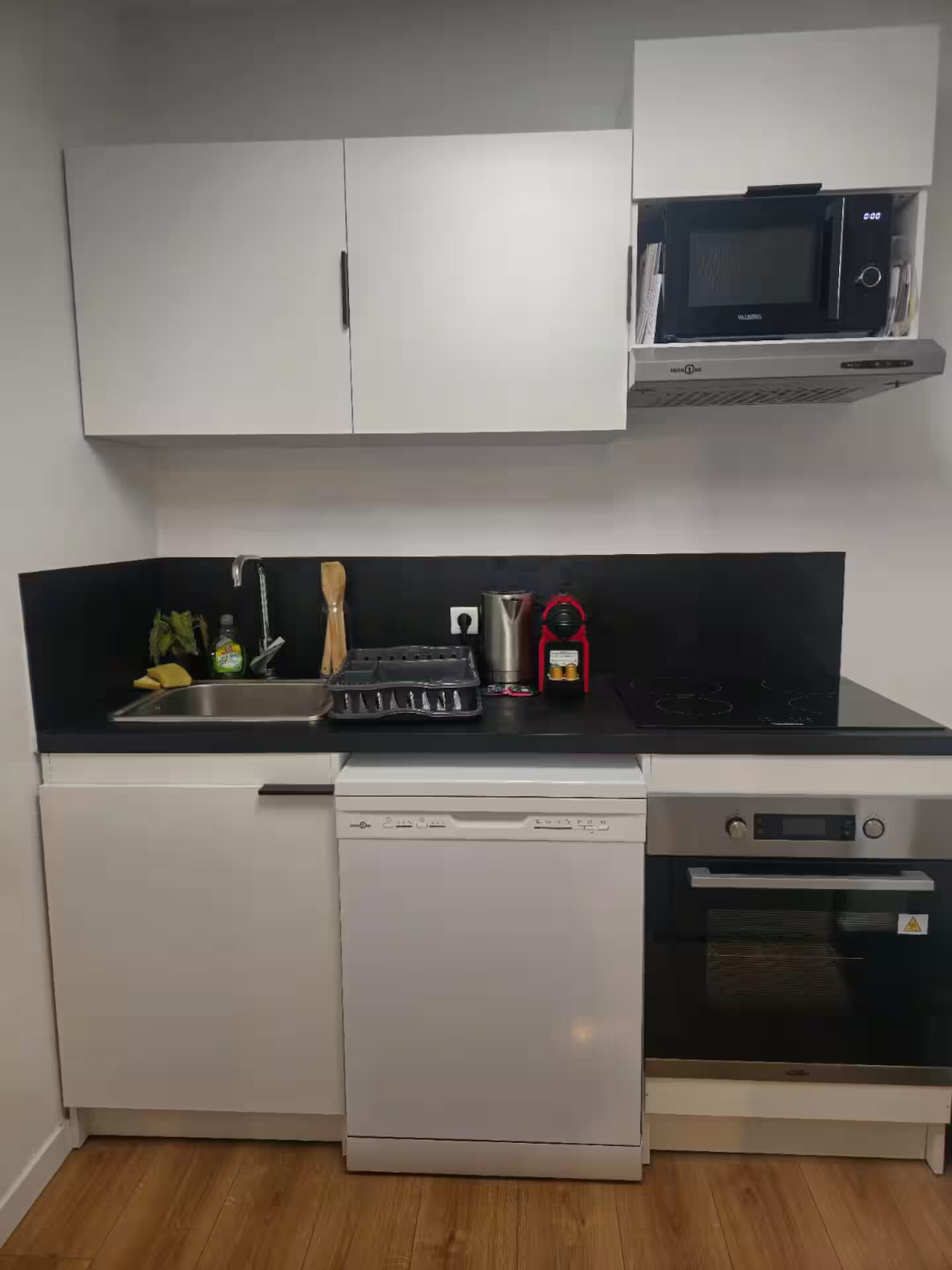 A compact kitchen with a dishwasher, stove, microwave, and a sink with various utensils.