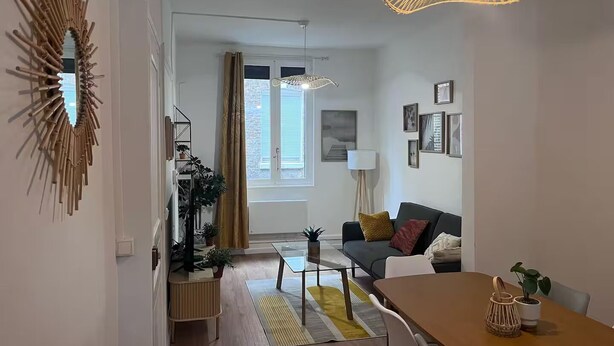 A modern living room with a sofa, a dining table, a hanging light fixture, and a decorative mirror.