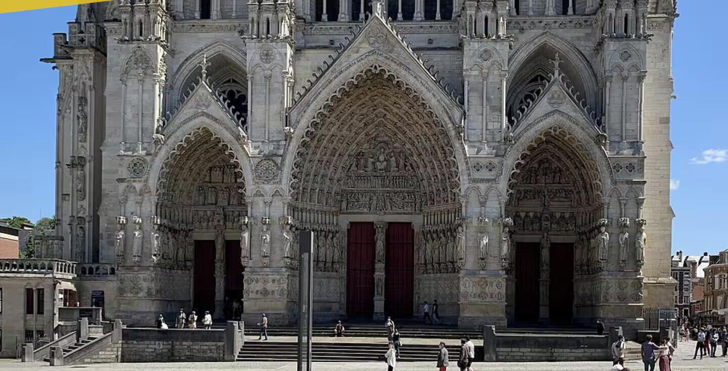 Une cathédrale de style gothique, ornée de sculptures complexes en pierre et dotée de grandes portes rouges.