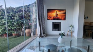 Moderni olohuone, jossa on lasipöytä, Buddha-aiheinen taulu ja ruokailutila, jossa on puiset tuolit.