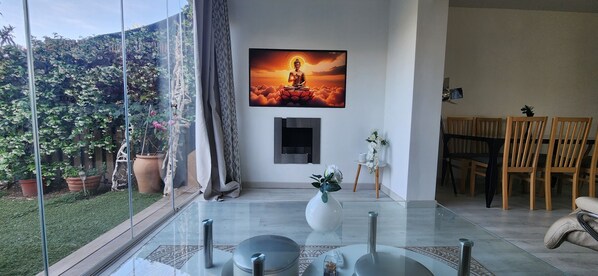 Ett modernt vardagsrum med ett glasbord, en målning av Buddha och en matplats med trästolar.