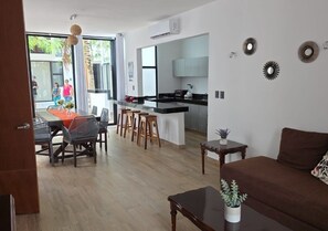 A modern living room with a sofa, a dining area with chairs and a table, and a kitchen area with a counter and stools. - Telchac 3 Bedrooms + pool and beach (Mérida)