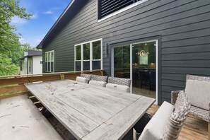 A patio with a wooden table and wicker furniture, a sliding glass door, and a view of a house with dark siding. - Rooftop Skyline Retreat w. Beltline Access (Atlanta)