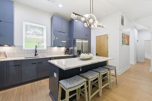 A modern kitchen with dark blue cabinets, a marble island with bar stools, and a pendant light. - Rooftop Skyline Retreat w. Beltline Access (Atlanta)