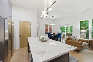 A modern kitchen with a marble island, stainless steel appliances, and a dining area with blue chairs. - Rooftop Skyline Retreat w. Beltline Access (Atlanta)