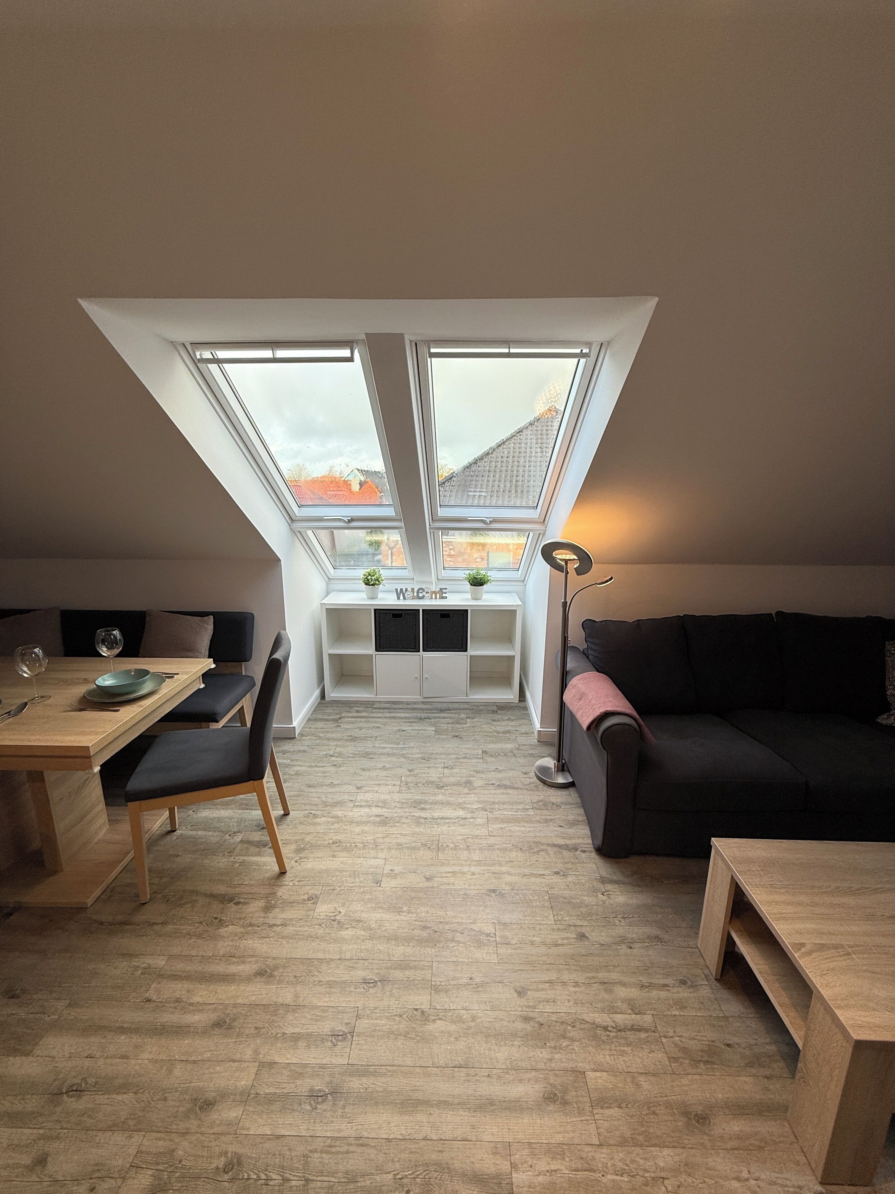 Ein Loft-Zimmer mit Esstisch, Stühlen, einer Couch, einer Stehlampe und einem Oberlicht.