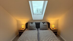 A room with a skylight, two beds with checkered bedding, bedside lamps, and a dark headboard.