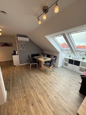 A modern loft bedroom with a sloped ceiling, skylight, and a dining area with a wooden table and chairs. - Vrbo Property (Wittmund)