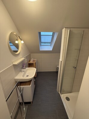 A modern bathroom with a skylight, a shower, and a vanity with a mirror. - Vrbo Property (Wittmund)