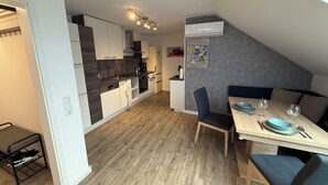 A modern kitchen with white and black cabinetry, a dining area with a wooden table and blue chairs, and a grey accent wall.