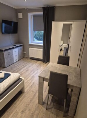 Een moderne kamer met een bed, een bureau, een stoel, een kledingkast, een televisie en een raam met gordijnen.