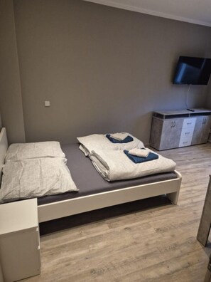 Ein Schlafzimmer mit einem Bett, einem an der Wand befestigten Fernseher und Holzboden.