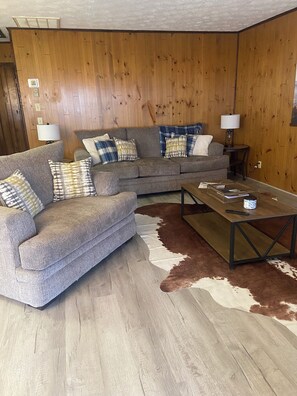 Ein Wohnzimmer mit grauem Sofa, einem Holztisch und einem Kuhfellteppich.