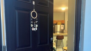 Uma porta preta com um sonho apanhador pendurado, dando acesso a uma cozinha com geladeira e mesa de jantar.