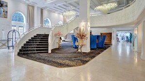 Um hall espaçoso com uma escadaria imponente, um candelabro e uma área de estar azul.
