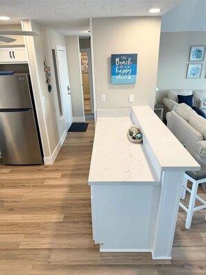 A modern kitchen with a built-in refrigerator, a white island, and a dining area with a sofa. - Beach Front - The Hamptons at Spanish Grant (Galveston)