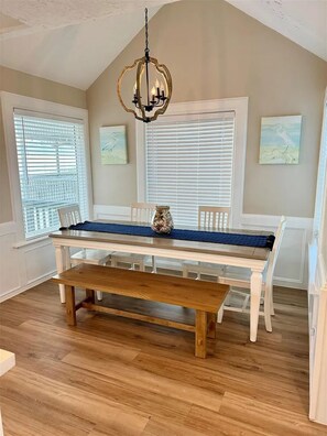 A dining area with a wooden bench, white table, and a chandelier. - Beach Front - The Hamptons at Spanish Grant (Galveston)