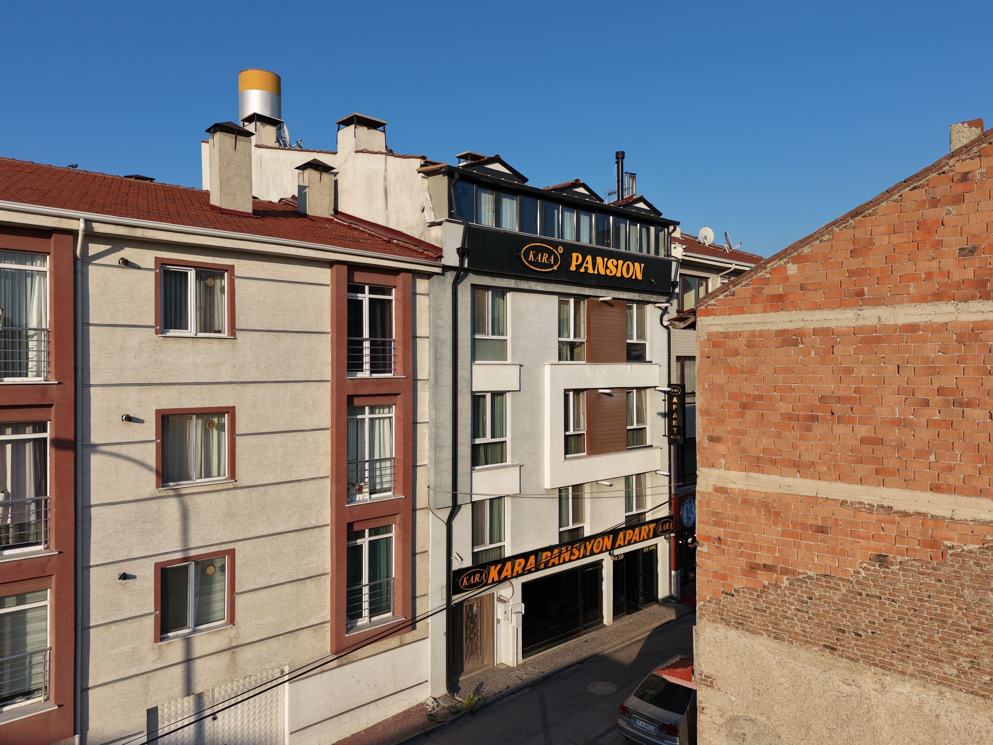 Un immeuble à plusieurs étages, sur lequel on peut lire l’inscription « KARA PANSION », indiquant qu’il s’agit d’un hôtel ou d’un ensemble d’appartements.