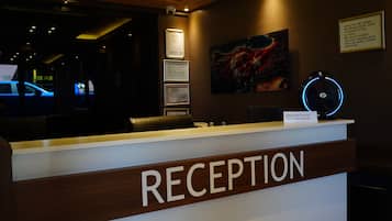 Un comptoir d’accueil avec une pancarte indiquant « RÉCEPTION », un certificat encadré, une horloge et un tableau accroché au mur.