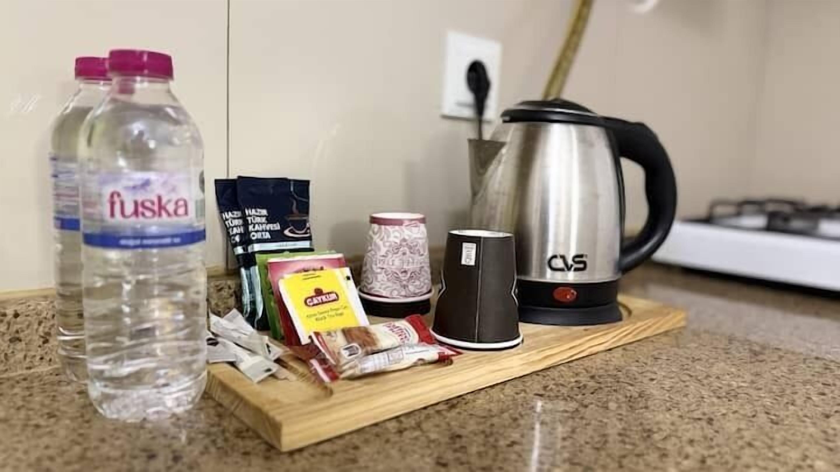 Uma bancada de cozinha com uma garrafa de água, caneca de café, saquinho de chá, sachê de chá e uma chaleira.