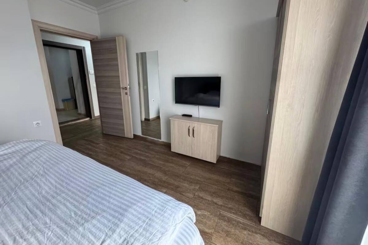 Una habitación de hotel con una cama, un televisor sobre un mueble de madera, un espejo y una puerta que da a otra habitación.