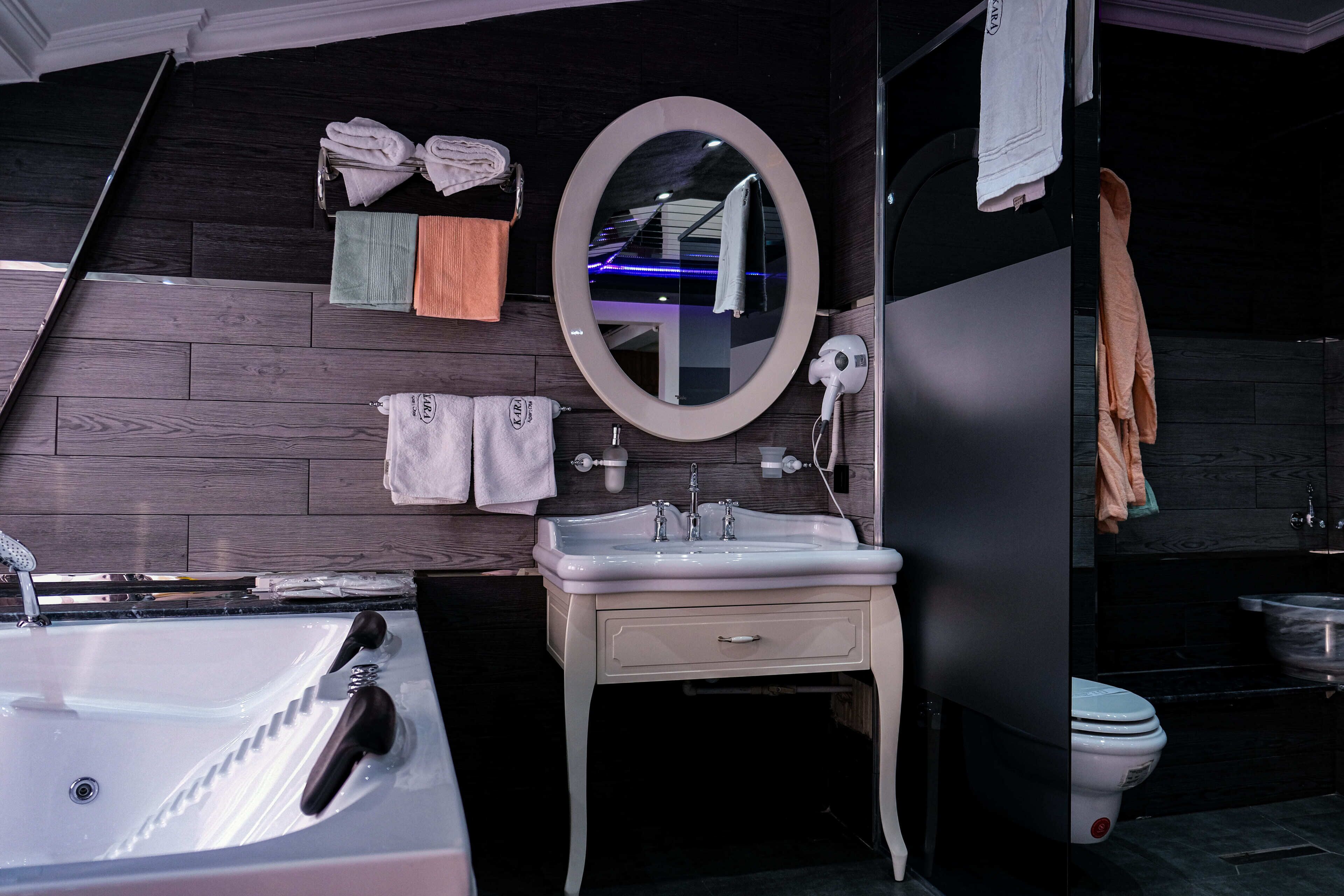 Une salle de bain moderne avec un lavabo blanc, un miroir rond et un mur en bois foncé.
