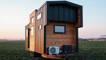 A small, modern, wooden cabin with a flat roof, large windows, and an air conditioning unit.