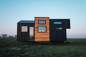 Ein modernes, kompaktes Mobilheim mit Holzfassade, großen Fenstern und flachem Dach, gelegen auf einem Feld.