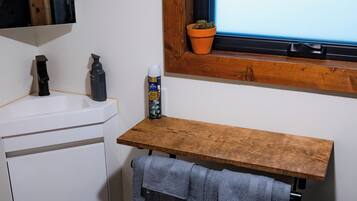 A bathroom with a white sink, wooden shelf, and a window with a view.