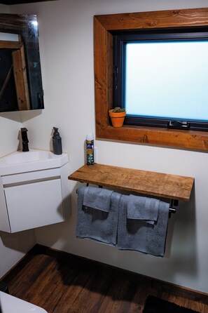 Un baño con lavamanos blanco, repisa de madera y ventana con vistas.