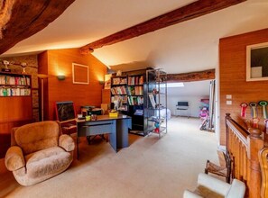 Een knus loft met zichtbare houten balken, een bureau, boekenkasten en een comfortabele fauteuil.