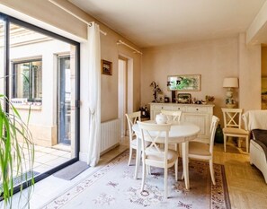A dining area with a table and chairs, a radiator, a cabinet, and a window with curtains. - Vrbo Property (Agen)