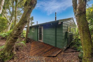 Eine kleine, grüne Holzhütte mit einer Holzterrasse, umgeben von Bäumen.