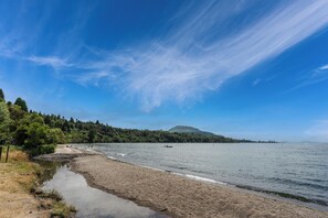 Uma praia com céu claro, águas calmas e uma colina ao longe.