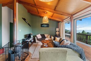 Een gezellige woonkamer met een open haard, een bank, een bijzettafeltje en een groot raam met uitzicht op de natuur.