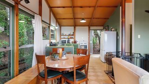 Een eetgedeelte met een houten tafel, stoelen en uitzicht op een keuken en tuin.