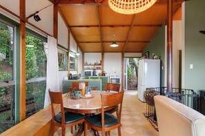 Uma sala de jantar com uma mesa de madeira, cadeiras e vista para uma cozinha e um jardim.