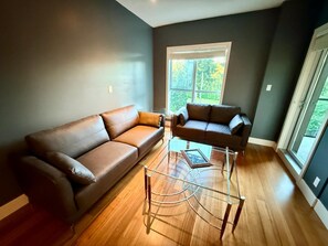 A modern living room with two leather sofas, a glass coffee table, and large windows with a view of trees. - Resort-Style Condo In a Prestigious Golf Community (Victoria)