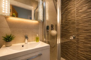 A bathroom with a white sink, a mirror with lights, a shower with a wooden wall, and a potted plant. - Cosy Modern, seconds from Shenfield Elizabeth Line (Shenfield)