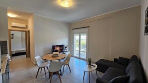 Ein Wohnzimmer mit Fernseher, einem Esstisch mit Stühlen, einer Couch und einer Glastür zum Außenbereich.