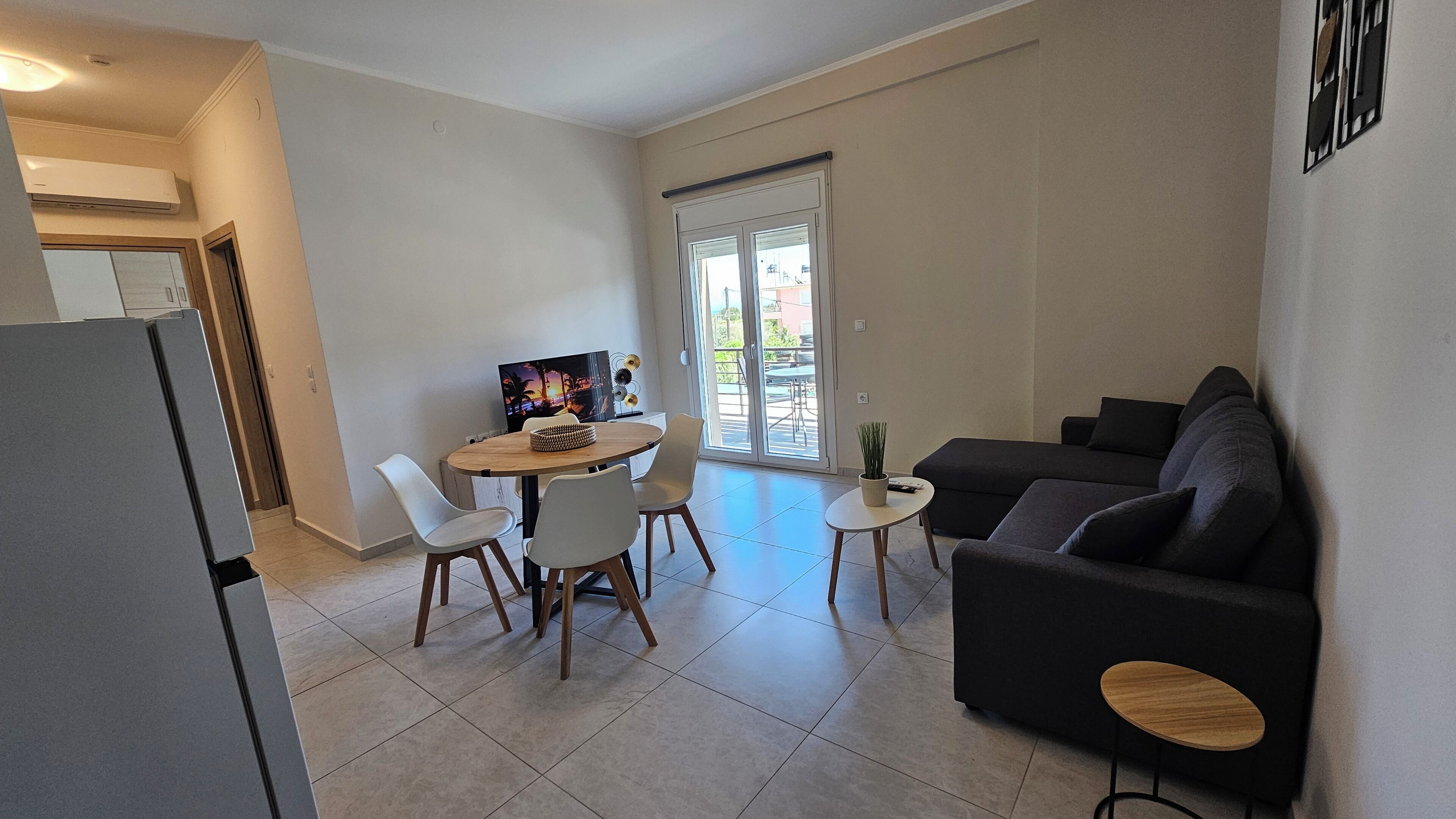 A modern living room with a dark sofa, a round table with chairs, a small side table, and a television.