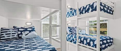 A bunk bed room with a nautical theme, featuring a blue and white color scheme and a window with blinds.