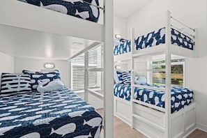 A bunk bed room with a nautical theme, featuring a blue and white color scheme and a window with blinds.